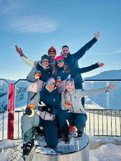 Gruppe auf einer Sonnenterrasse im Schnee, die Arme in der Luft