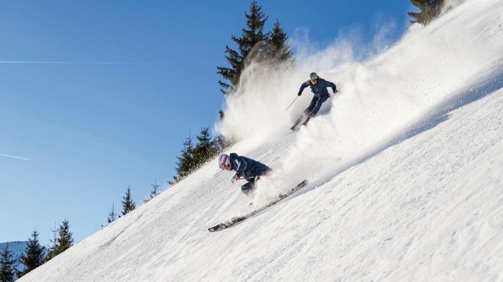 Zwei Skifahrer in Schwüngen einen sonnigen Hang hinunter