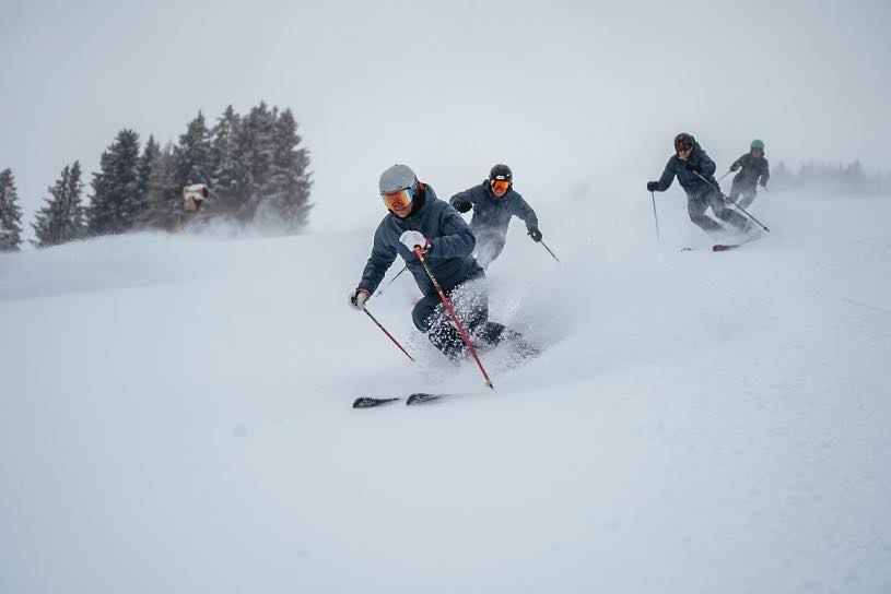 Drei Skifahrer im Tiefschnee vor verschneiten Bäumen
