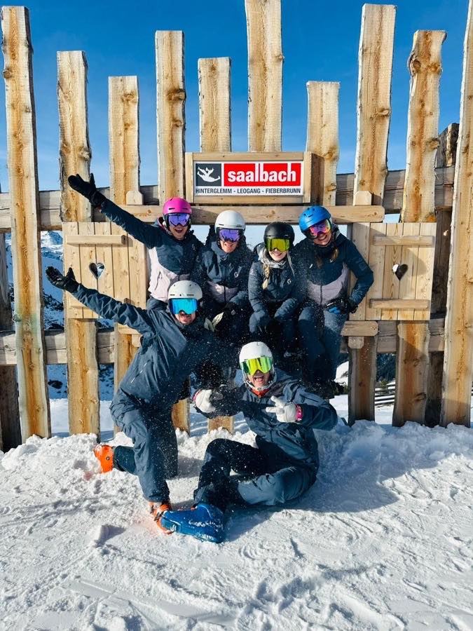 Gruppe am Ortsschild Saalbach, eine Person sitzt im Schnee